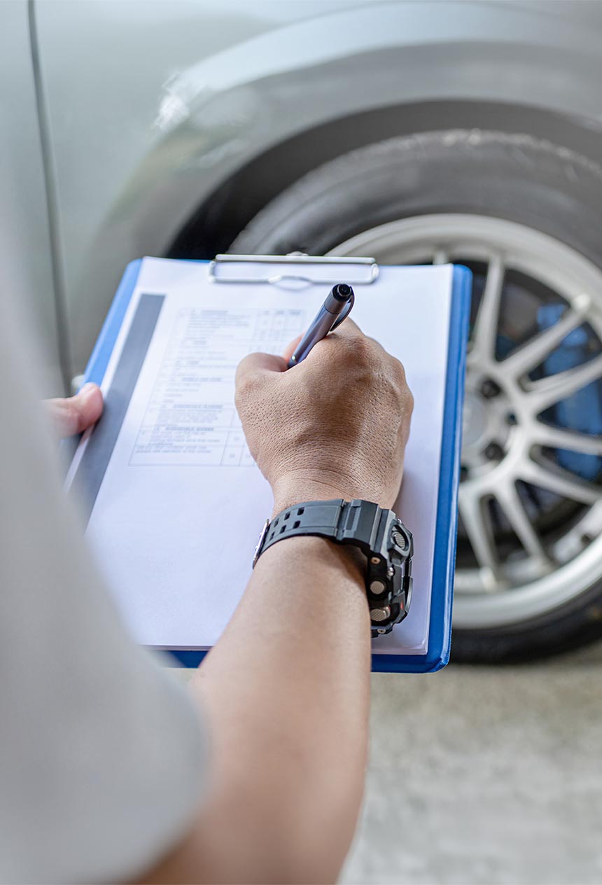 Mills Collision Center technician with clipboard inspecting vehicle damage